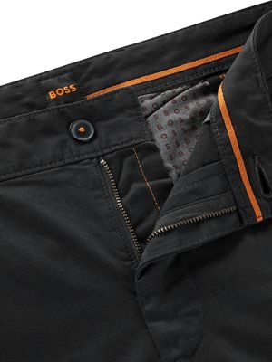 Nahaufnahme von schwarzer Hose mit geöffnetem Reißverschluss. Der Bund zeigt das BOSS-Logo in Orange. Auf der Innenseite ist ein Stoff mit BOSS-Logo-Muster sichtbar. Ein Knopf ist ebenfalls vorhanden.