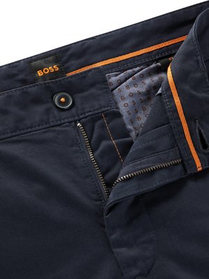 Nahaufnahme einer dunkelblauen Hose. Der Reißverschluss ist geöffnet. Der Hosenbund weist einen Knopf und das Markenlogo "BOSS" auf. Orangene Akzente sind sichtbar. Innenfutter mit Logo.