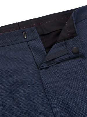 Nahaufnahme einer dunkelblauen Hose. Der Reißverschluss ist halb geöffnet, ein Knopf und ein Hosenhaken sind zu sehen. Der Hosenbund ist teilweise schwarz mit roter Naht. Der Stoff hat ein feines Muster.