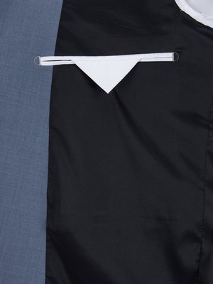 Nahaufnahme eines Sakkos. Blaue Stoffseite links, schwarzes Innenfutter rechts. Ein weißes Stoffdreieck ragt aus einer weißen Tasche im schwarzen Futter hervor. Der Saum der Tasche ist sichtbar.