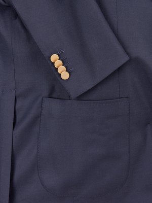 Nahaufnahme eines dunkelblauen Sakkos. Der Ärmel ist angewinkelt und zeigt vier helle Knöpfe. Die Brusttasche ist sichtbar. Das Sakko ist aus einem glatten Stoff gefertigt.