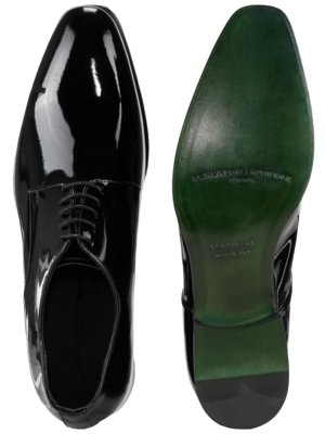 Zwei schwarze Lacklederschuhe vor weißem Hintergrund. Der linke Schuh ist von oben, der rechte von unten zu sehen. Die Schuhsohle ist grün und hat eine Aufschrift. Beide Schuhe haben Schnürsenkel.