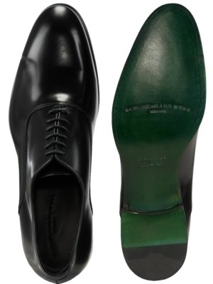 Zwei schwarze Lederschuhe, Ansicht von oben. Links ist ein Schuh mit Schnürsenkeln zu sehen. Rechts die grüne Ledersohle des zweiten Schuhs mit Schrift.