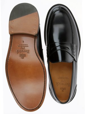 Zwei schwarze Loafers Schuhe, einer von unten mit Ledersohle, der andere von oben. Auf der Sohle ist "Berwick" und Schuhgröße 8 eingeprägt. Der andere Schuh hat glänzendes Oberleder.