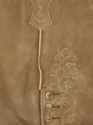 Nahaufnahme eines braunen Leder Kleidungsstücks mit gestickten floralen Mustern. Oben eine spitze Applikation und eine vertikale Naht. Drei runde Knöpfe aus Naturmaterial. Das Leder ist leicht strukturiert und hat eine matte Oberfläche.