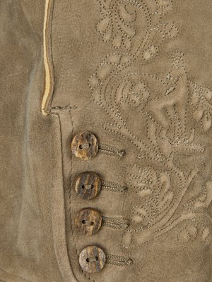 Nahaufnahme von braunem Leder mit drei Knöpfen aus Holz und Zierstichen. Auf dem Leder sind florale Muster gestickt, die Knöpfe sind mit Knopflöchern verbunden. Eine Naht verläuft entlang der linken Seite.