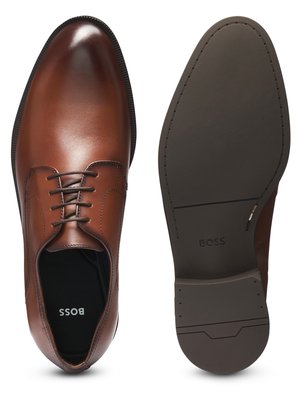 Zwei braune Lederschuhe, einer von oben, der andere mit der Sohle nach oben gezeigt. Der Schuh von oben hat Schnürsenkel und das Logo "BOSS" in der Innensohle. Auf der Sohle des anderen Schuhs ist das Logo "BOSS" zu sehen.