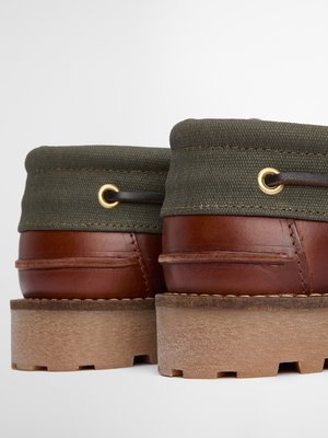 Zwei braune Lederschuhe mit hellbraunen Sohlen. Die Schuhe haben grüne Stoffbündchen mit Ösen. Die Schuhe stehen nebeneinander auf weißem Hintergrund und sind im Detail dargestellt.