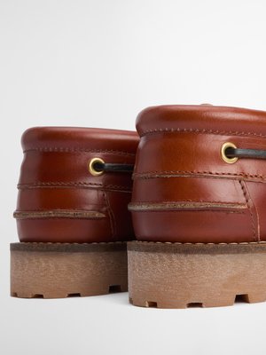 Zwei braune Lederschuhe mit hellbraunen Sohlen, Blick auf die Rückseite. Die Schuhe haben goldfarbene Ösen, durch die eine dunkle Schnur verläuft. Der Hintergrund ist weiß.