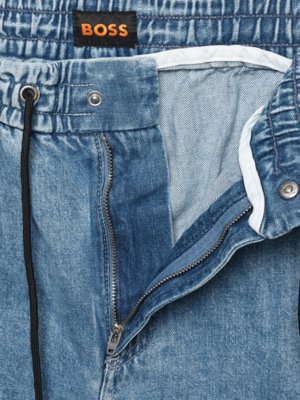 Nahaufnahme von hellblauen Jeans. Ein schwarzer Kordelzug mit Öse, der Bund ist gerafft. Ein Reißverschluss öffnet die Jeans. Der Markenname "BOSS" ist auf einem Etikett aufgedruckt.