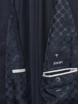 Nahaufnahme eines dunklen Anzugs. Innenfutter mit floralem Muster. Auf einem Etikett ist das JOOP!-Logo abgebildet. Anzug hat eine Innentasche und einen Knopf mit der Aufschrift "SLIM FIT". Die Naht ist weiß.