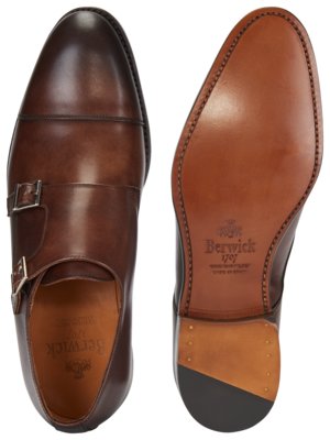 Zwei braune Herrenschuhe auf weißem Hintergrund. Einer der Schuhe von der Seite mit zwei Schnallen, der andere von unten mit der Marke Berwick. Die Sohle ist hellbraun.