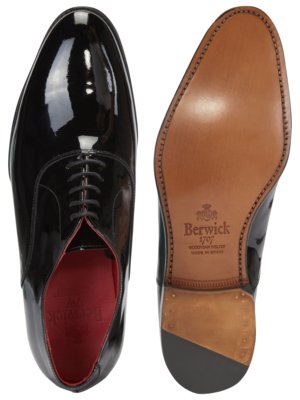 Zwei Ansichten eines schwarzen Lacklederschuhs. Der linke Schuh ist von oben gesehen und zeigt Schnürsenkel und rote Innensohle. Der rechte Schuh zeigt die braune Ledersohle mit eingeprägtem Berwick-Logo.