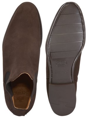 Zwei braune Wildlederstiefel, Draufsicht. Der linke Stiefel zeigt die Oberseite, der rechte die Sohle. Die Sohle hat ein geprägtes Profil und Label. Der linke Stiefel hat einen elastischen Einsatz und eine Innensohle mit Logo.