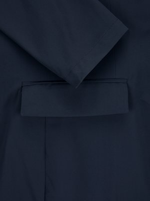 Nahaufnahme eines dunkelblauen Anzugs. Der Ärmel eines Blazers ist sichtbar, zusammen mit einer aufgesetzten Tasche. Das Bild zeigt einen Ausschnitt des Anzugs, der aus Stoff besteht.