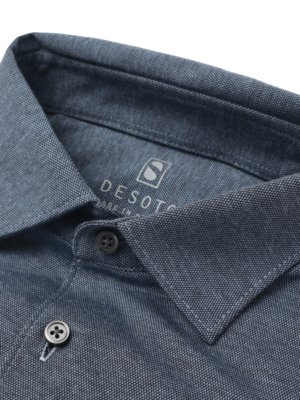 Nahaufnahme eines blauen Polohemdes. Kragen, Knopfleiste mit zwei Knöpfen sichtbar. Im Kragen steht "DESOTO". Stoffstruktur ist erkennbar, vor weißem Hintergrund.