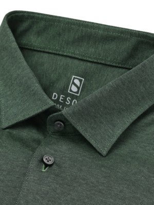 Nahaufnahme eines dunkelgrünen Polo-Hemdkragens. Der Kragen ist hochgeklappt und mit zwei Knöpfen versehen. Ein Logo mit einem "S" in einem quadratischen Rahmen ist sichtbar. Der Stoff weist eine feine Textur auf.