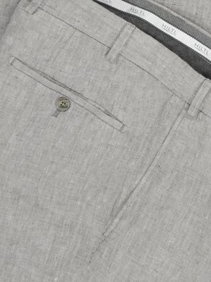Naheinstellung einer hellgrauen Leinenhose. Ein Teil der Hosentasche mit Knopf ist sichtbar. Der Bund ist teilweise zu sehen, mit dem Logo "HILTL" auf weißem Band. Das Material scheint grob gewebt zu sein.