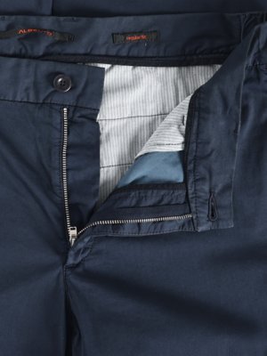 Nahaufnahme einer geöffneten, dunkelblauen Hose. Der Reißverschluss ist teilweise geöffnet. Innen ist ein weiß-grau gestreifter Stoff zu sehen. Ein Knopf und ein kleines eingenähtes Etikett sind am Bund sichtbar.