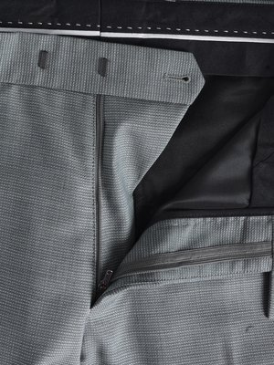 Nahaufnahme einer grauen Stoffhose mit verdecktem Reißverschluss. Der Hosenbund ist mit zwei Knöpfen und einem Knopf versehen. Der Stoff hat ein kleines, gepunktetes Muster. Der Hosenlatz ist teilweise geöffnet, der Innere Stoff ist schwarz.