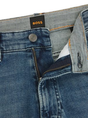 Nahaufnahme einer Jeanshose in Blau. Der Reißverschluss ist geöffnet, und ein Knopf ist sichtbar. Oberhalb des Hosenbundes befindet sich ein schwarzes Label mit dem Wort „BOSS“ in orangefarbenen Buchstaben. Die Naht ist orange gefärbt.