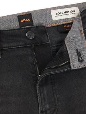 Nahaufnahme einer schwarzen Jeans. Der Hosenbund ist mit einem Reißverschluss und einem Knopf versehen. Über dem Hosenbund befinden sich zwei Etiketten mit der Aufschrift "BOSS" und "SOFT MOTION".