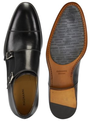 Draufsicht auf einen schwarzen Lederschuh mit zwei Schnallen und einem anderen Schuh. Der andere Schuh zeigt die Sohle mit dem Markennamen Magnanni und "Made in Spain" darunter.