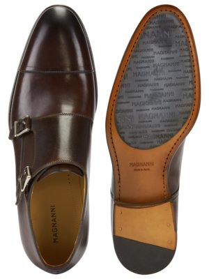 Zwei braune Lederschuhe auf weißem Hintergrund. Der linke Schuh ist ein Doppelmonk-Schuh. Der rechte Schuh ist umgedreht und zeigt die Sohle, die mit MAGNANNI Schrift bedeckt ist.
