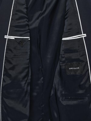 Draufsicht auf die Innenseite eines dunkelblauen Sakkos. Die Innenseiten sind mit schwarzem Stoff ausgekleidet. Auf der rechten Seite befindet sich ein eingenähtes Label mit dem Wort "Dressler". Taschen und weiße Nähte sind erkennbar.