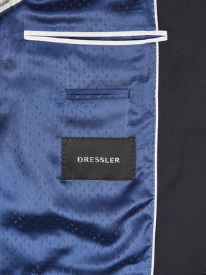Nahaufnahme des Innenfutters eines schwarzen Sakkos. Blaues Innenfutter mit dezentem Muster. Rechteckiger schwarzer Aufnäher mit weißem Schriftzug "DRESSLER". Oben eine Innentasche und weißer Streifen als Zierde.