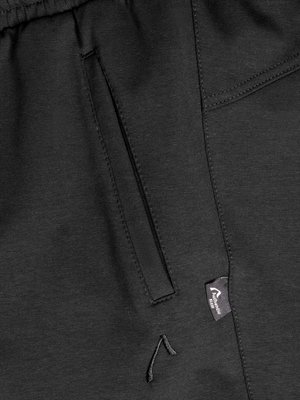 Detailaufnahme einer schwarzen Hose aus Stoff. Eine senkrechte Naht teilt das Bild in zwei Teile. Links eine senkrechte Eingrifftasche, rechts eine rechteckige Tasche. Unten links gesticktes Motiv, rechts Label.