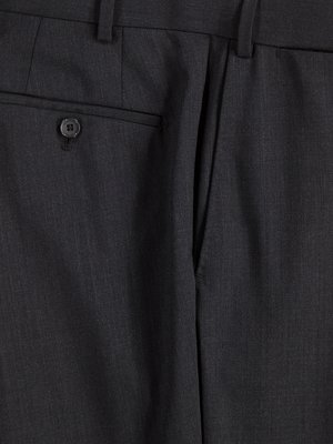 Nahaufnahme einer dunkelgrauen Hose. Ein Knopf an einer Gesäßtasche ist zu sehen, sowie die Naht zum Hosenschlitz und die vertikalen Streifen des Stoffes. Die Hosentasche ist offen.