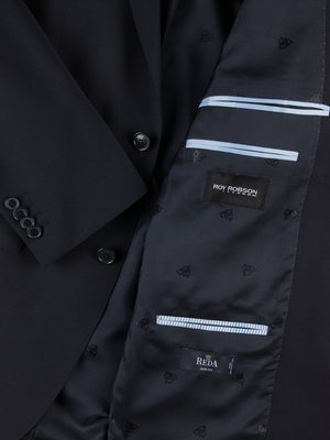 Nahaufnahme eines dunkelblauen Anzugs. Die Innenseite des Anzugs ist sichtbar, mit einem blauen Futter, in dem kleine Logos abgebildet sind. Auf dem Futter sind Markenlogos und Details zu sehen. Die Knöpfe des Anzugs sind ebenfalls sichtbar.