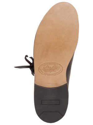 Ansicht von unten eines schwarzen Lederschuhs. Man sieht die helle Lederinnensohle mit Prägung eines Logos. Der Schuh hat eine dunkle Gummiabsatz und Schnürsenkel.